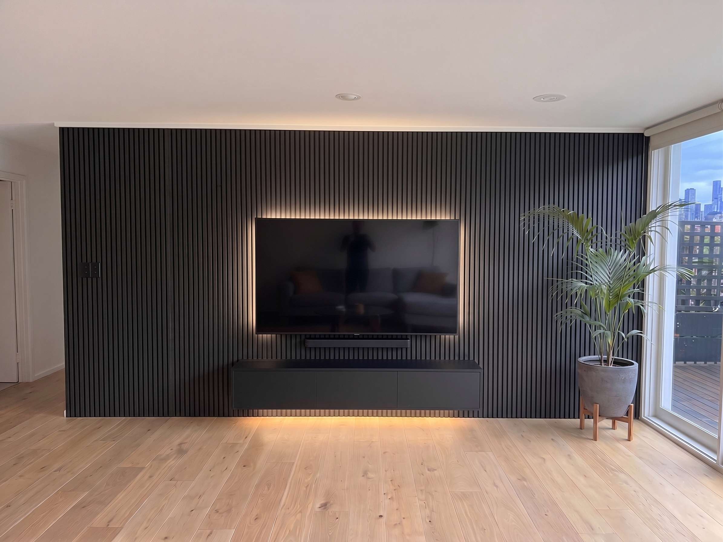Black acoustic timber feature wall with recessed TV and LED backlighting in a Melbourne living room